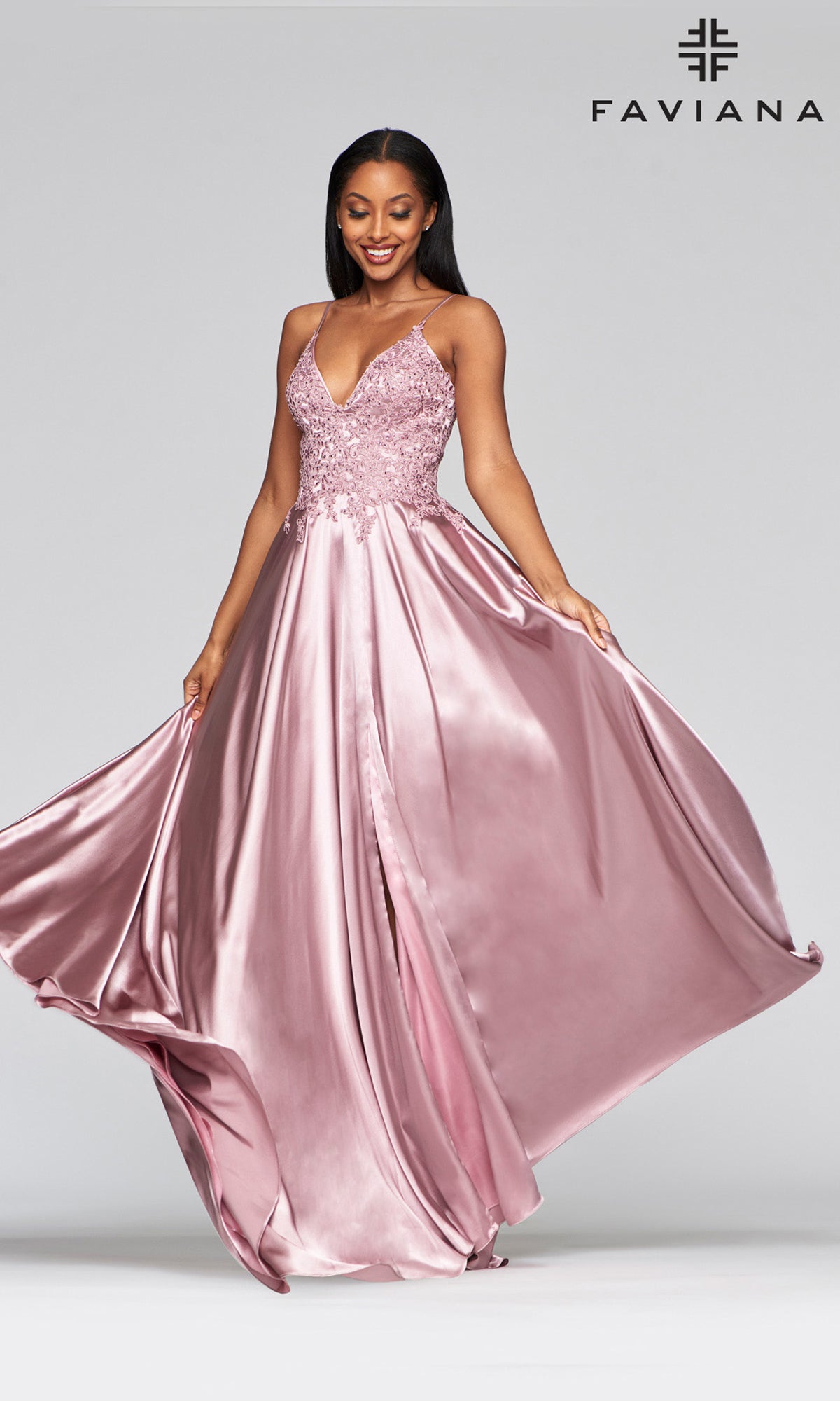 A woman stands against a plain background, wearing the Faviana Lace-Bodice Long A-Line Prom Dress—a sleeveless blush pink gown with an embroidered lace bodice and flowing satin skirt. The Faviana logo appears in the top right corner.